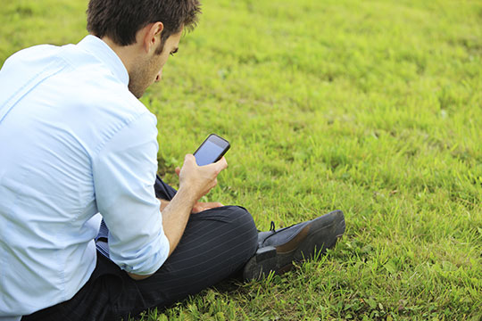 male is checking his phone while sitting on the grass