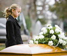 Sad little girl dressed in black standing in front of casket