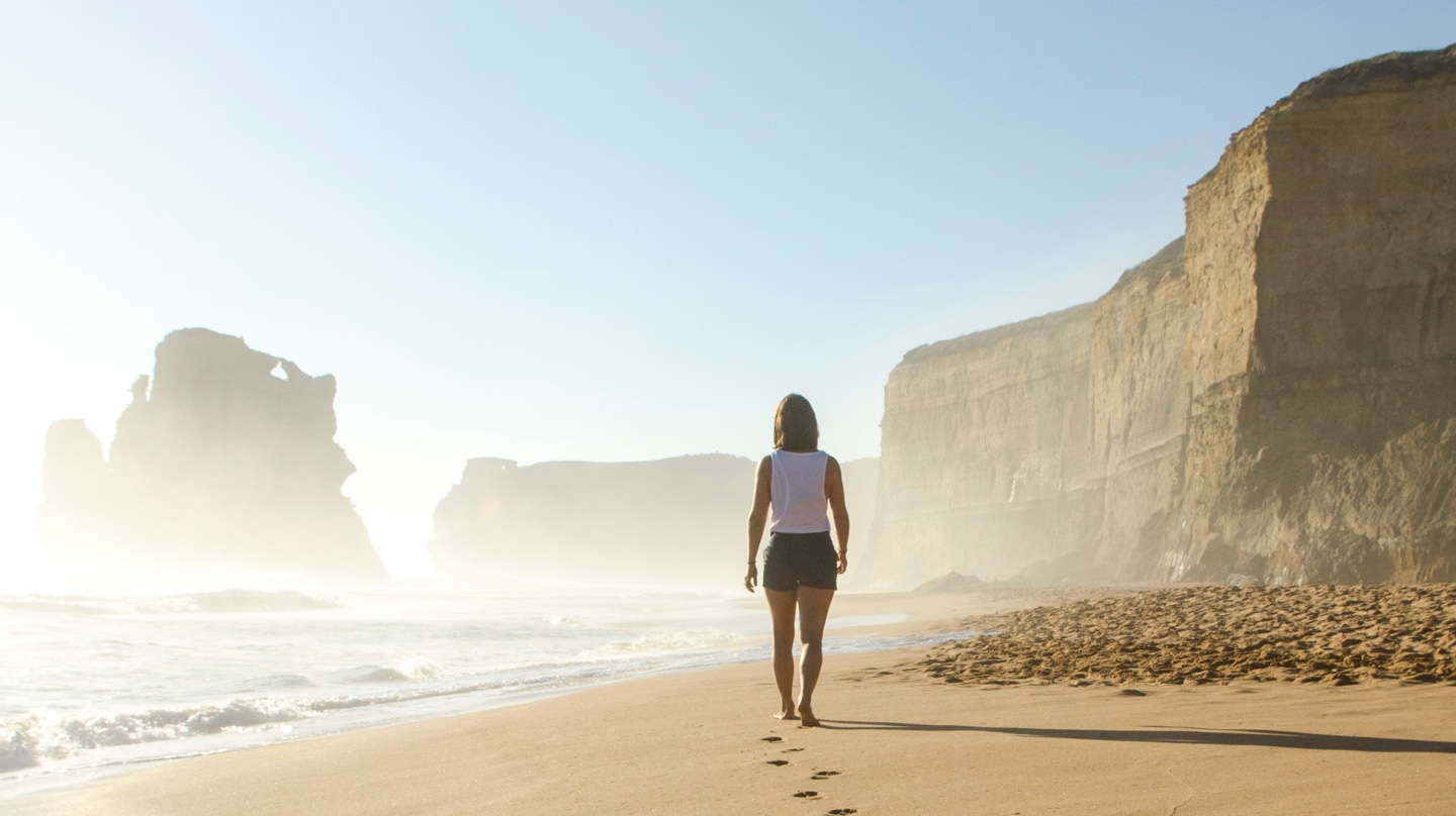 Woman walking on the beach, leaving footsteps in the sand.